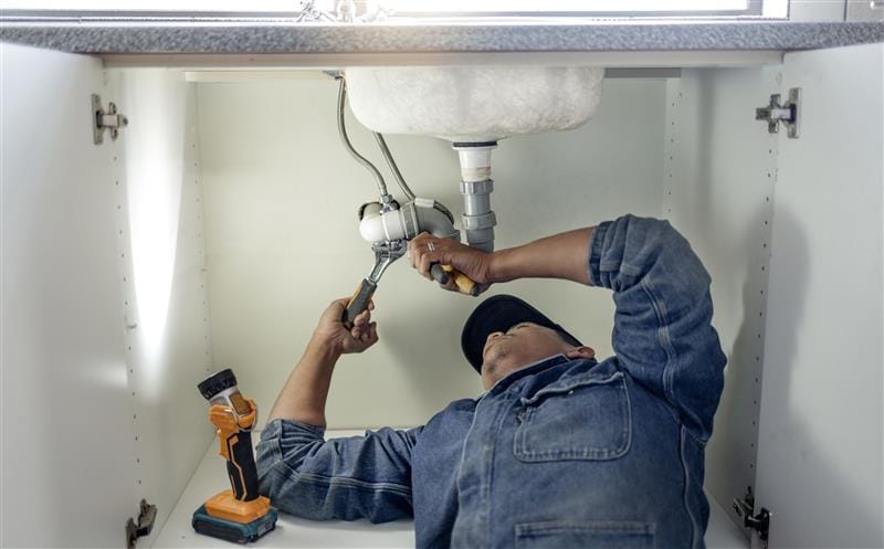 Plumber repairing pipes beneath a bathroom sink in Redmond