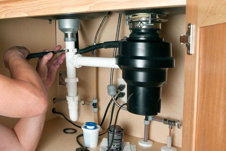 Plumber installing a garbage disposal beneath a kitchen sink in Redmond
