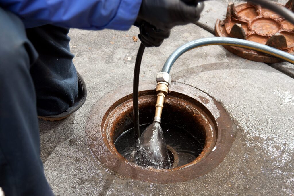Plumber hydro jetting a sewer line through a manhole in Redmond