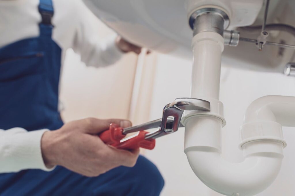Plumber repairing a white drain pipe beneath a sink in Redmond