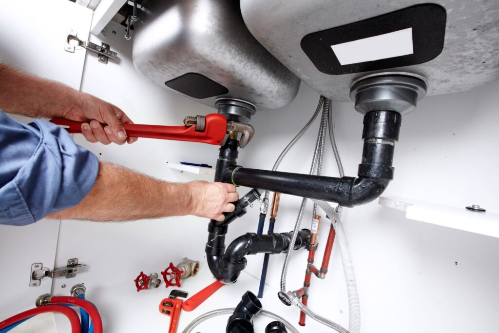 Plumber repairing drain pipes beneath a kitchen sink in Redmond
